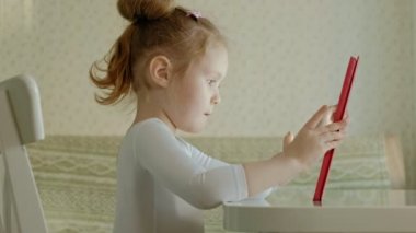 mutfak veya Oda masada oturan ve bir tablet bilgisayar kullanarak oynayan sevimli küçük kız. Örümcek ağı dalga köpüğü.