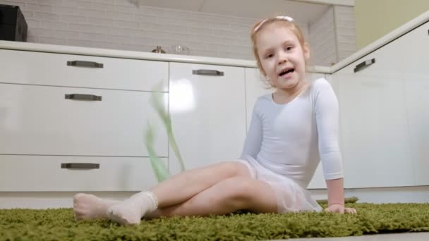 Een gelukkig meisje in een witte gymnastische zwembroek treinen, dansen met een lint voor ritmische gymnastiek, sprongen en uitvoeren van professionele oefeningen. — Stockvideo