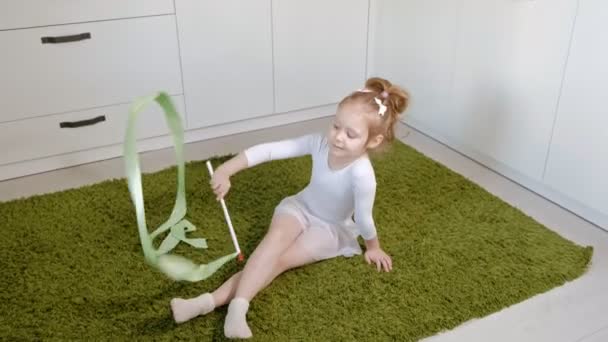 Una bambina felice in costume da bagno bianco da ginnastica, balli con nastro per ginnastica ritmica, salti ed esercizi professionali . — Video Stock