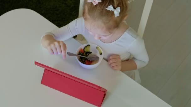 Meisje eet en speelt met behulp van computer tablet. surfen op het web — Stockvideo