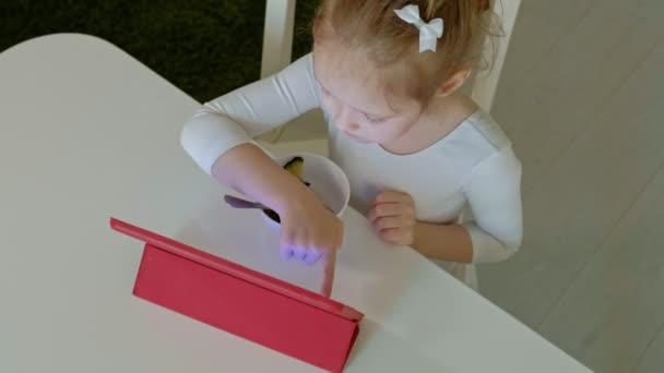 Niña come y juega con la tableta de la computadora. navegación en la web — Vídeo de stock