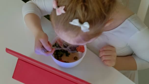 Meisje eet en speelt met behulp van computer tablet. surfen op het web — Stockvideo