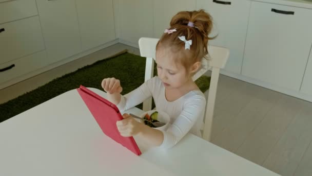 Little girl eats and plays using computer tablet. web surfing — Stock Video