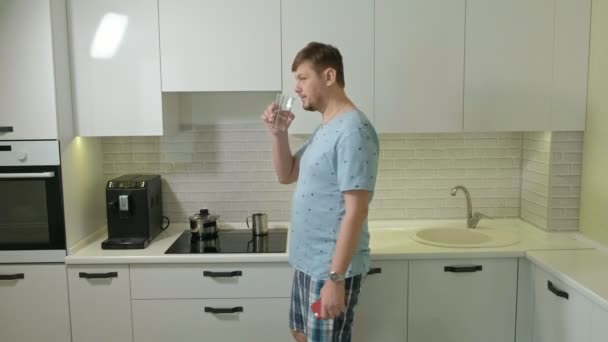 Un hombre en pijama bebiendo agua en la cocina. Buenos días. — Vídeos de Stock