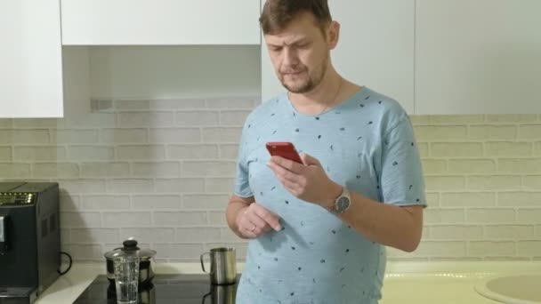 Un hombre en pijama bebiendo agua en la cocina. Buenos días. — Vídeos de Stock