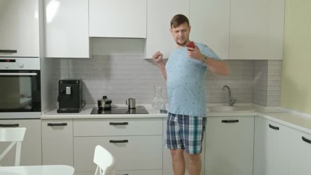 Un hombre en pijama bebiendo agua en la cocina. Buenos días. — Vídeos de Stock