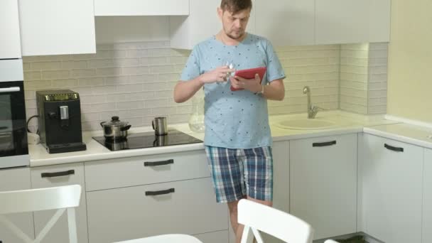 Un hombre en pijama bebiendo agua en la cocina. Buenos días. — Vídeos de Stock