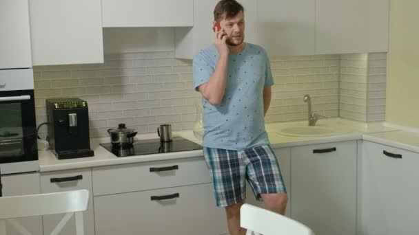 Un hombre en pijama bebiendo agua en la cocina. Buenos días. — Vídeos de Stock