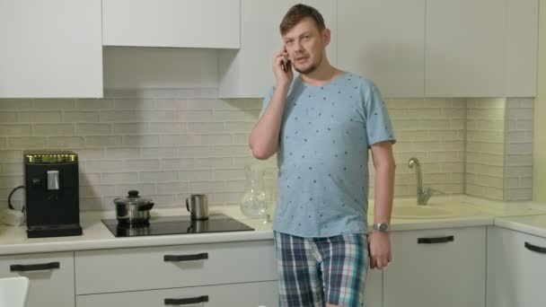 Un hombre en pijama bebiendo agua en la cocina. Buenos días. — Vídeo de stock