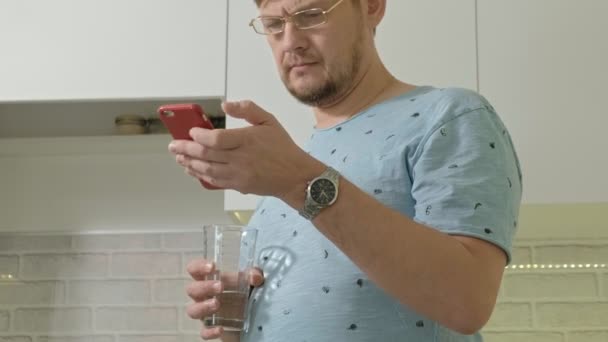 Een man in pyjama drinkwater in de keuken. Ochtend — Stockvideo