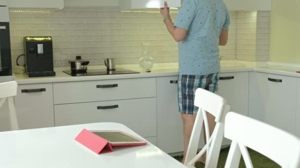 Un hombre en pijama bebiendo agua en la cocina. Buenos días. — Vídeo de stock