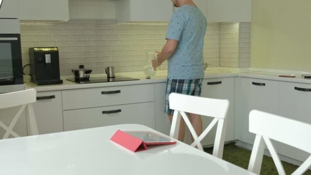 Um homem de pijama a beber água na cozinha. Bom dia. — Vídeo de Stock