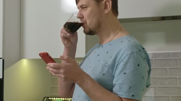 Un hombre en pijama bebiendo agua en la cocina. Buenos días. — Vídeos de Stock