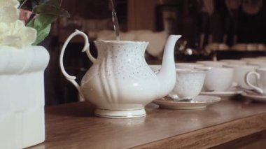 Bir adam ahşap masada beyaz bir bardak içine bir su ısıtıcısından çay dökülen.