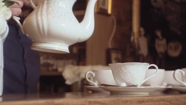 Een man giet thee uit een ketel in een witte kop op een houten tafel. — Stockvideo