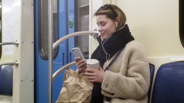 Ung brunett kvinna rider på kollektivtrafik, använder telefonen med hörlurar — Stockvideo