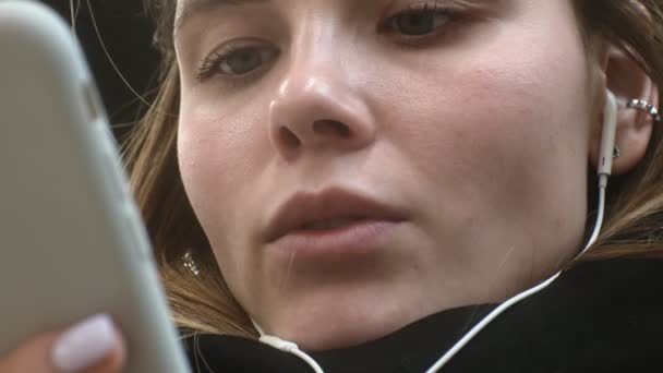Ung brunett kvinna använder en telefon med hörlurar — Stockvideo