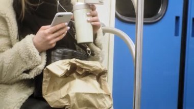 Genç esmer kadın toplu taşıma araçlarına biniyor, kulaklıkla telefonu kullanıyor.