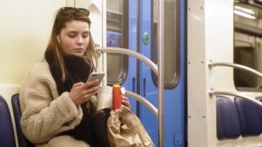 Genç esmer kadın toplu taşıma araçlarına biniyor, kulaklıkla telefonu kullanıyor.