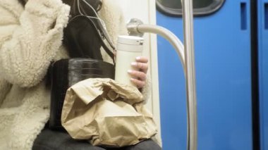 Genç esmer kadın toplu taşıma araçlarına biniyor, kulaklıkla telefonu kullanıyor.