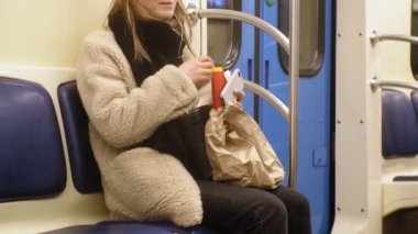 Genç esmer kadın toplu taşıma araçlarına biniyor, kulaklıkla telefonu kullanıyor.