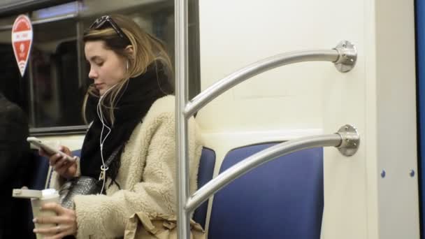 Young brunette woman rides on public transport, uses the phone with headphones — 비디오