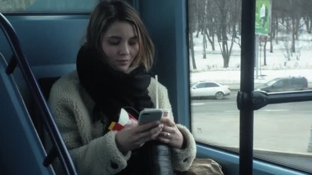 Young brunette woman rides on public transport, uses the phone with headphones — ストック動画