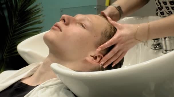Парикмахер моет голову мальчику в салоне — стоковое видео