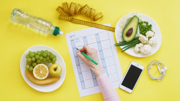 Een fitness kalender houden. concept van gezond eten, dieet, bovenaanzicht, gele achtergrond — Stockvideo