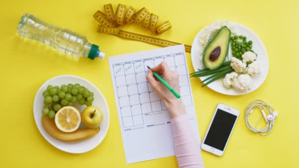 Hålla en träningskalender. begreppet hälsosam mat, kost, uppifrån, gul bakgrund — Stockvideo