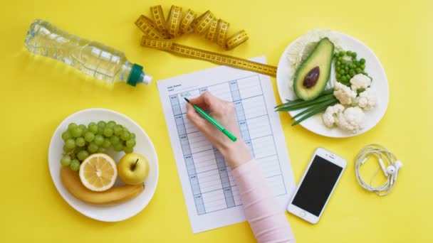 Een fitness kalender houden. concept van gezond eten, dieet, bovenaanzicht, gele achtergrond — Stockvideo