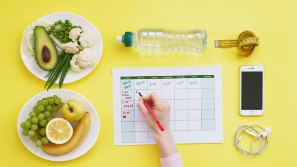 A fitness naptár vezetése. az egészséges táplálkozás fogalma, étrend, felülnézet, sárga háttér — Stock videók