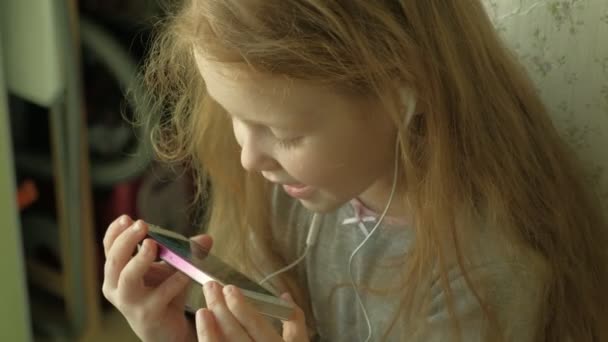 Little girl sitting on the window uses the phone — Stock Video