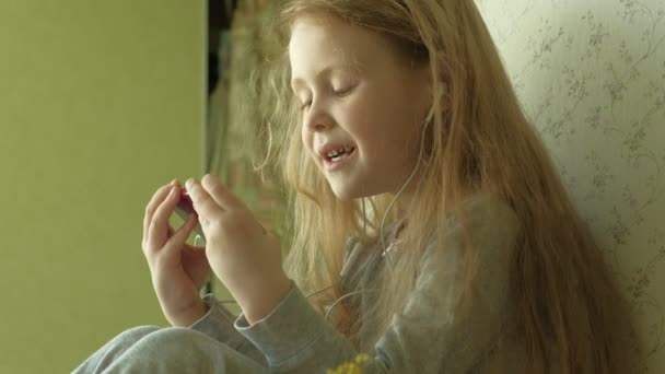 Kleines Mädchen, das am Fenster sitzt, benutzt das Telefon — Stockvideo