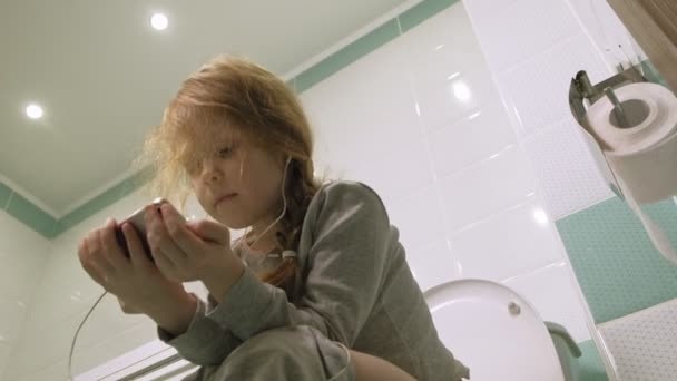 Mała dziewczynka siedzi w toalecie i korzysta z telefonu — Wideo stockowe