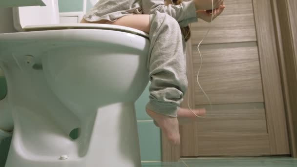 小さな女の子はトイレに座って、電話を使用しています — ストック動画