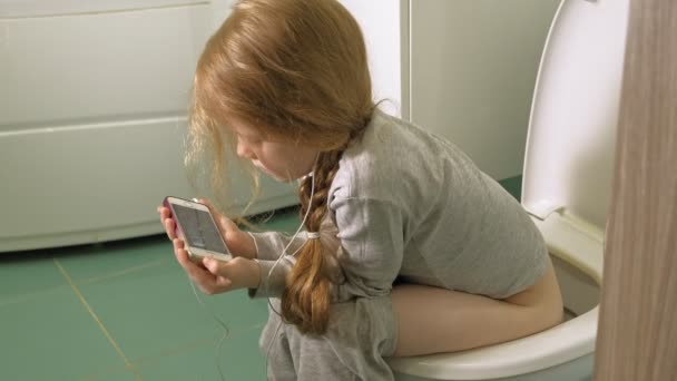 Bambina si siede sul water e utilizza il telefono — Video Stock