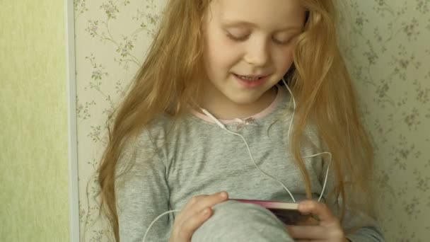 Klein meisje zittend op het raam maakt gebruik van de telefoon — Stockvideo