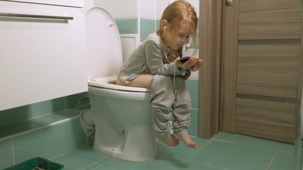 Little girl sits on the toilet and uses the phone — Stock Video