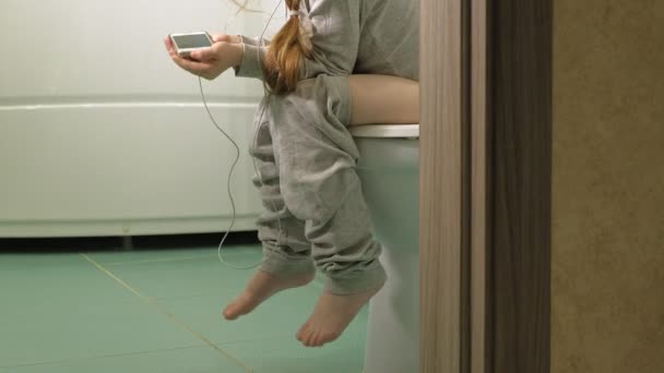 Küçük kız tuvalette oturur ve telefon kullanır — Stok video