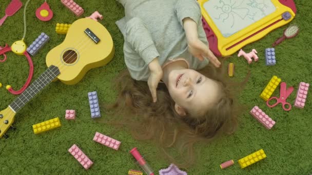 Маленька дівчинка сміється лежачи на зеленому фоні, вид зверху — стокове відео