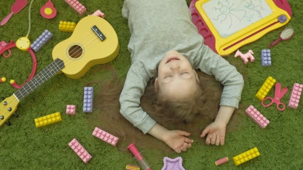 小さな女の子は緑の背景に横たわって笑う、トップビュー — ストック動画