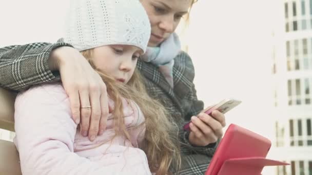 Donna con una bambina è seduto su una panchina e utilizzando gadget — Video Stock