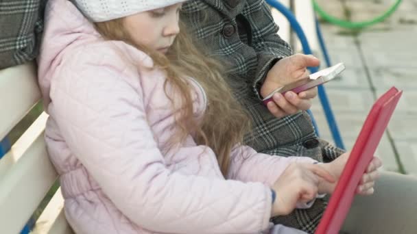 Mujer con una niña está sentado en un banco y el uso de gadgets — Vídeo de stock
