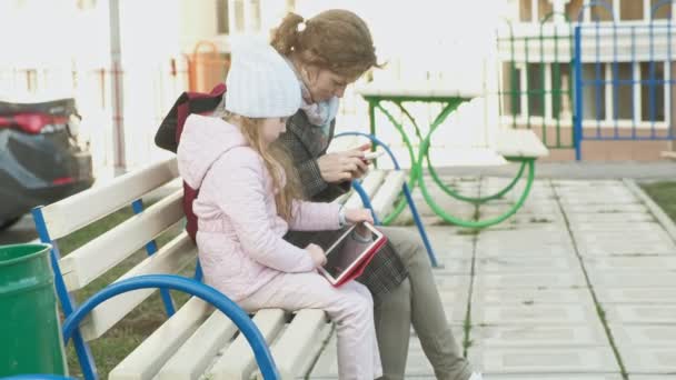 Mujer con una niña está sentado en un banco y el uso de gadgets — Vídeos de Stock