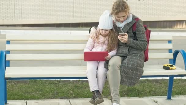 Vrouw met een klein meisje zit op een bankje en het gebruik van gadgets — Stockvideo