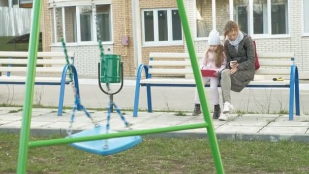 Woman with a little girl is sitting on a bench and using gadgets — Stock Video