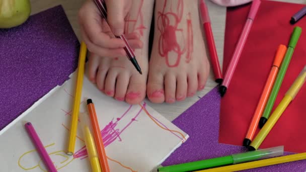 Маленькая девочка рисует на ногах ручками для войлока, детским творчеством, развитием — стоковое видео