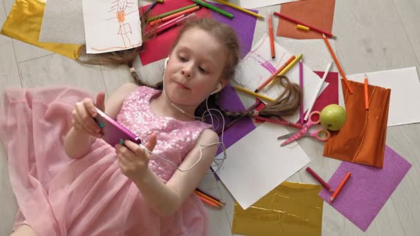Kleines Mädchen, das auf dem Boden liegt, telefoniert, hört Musik — Stockvideo