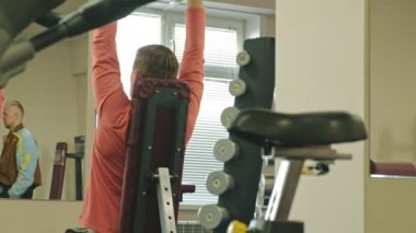 Bir adam bir fitness stüdyosunda düz bir kavrama ile oturan dumbbells ile bir bank basın yapıyor